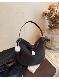 Detail view of coffee brown hobo bag with metal charm and white plush pompom accessory