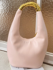 Pale pink hobo bag with asymmetric golden metal handle on a magazine backdrop