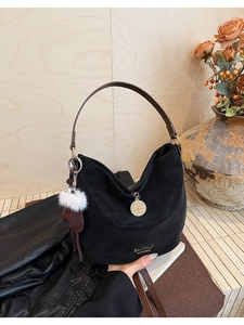 Detail of black suede tote bag featuring brown leather handle and white faux fur charm