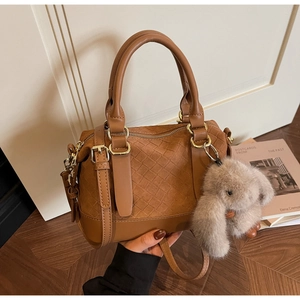 Detail of caramel brown woven leather pillow bag with a plush bunny charm attachment