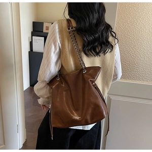 Close-up of brown glossy leather tote bag with silver chain strap and fashion logo