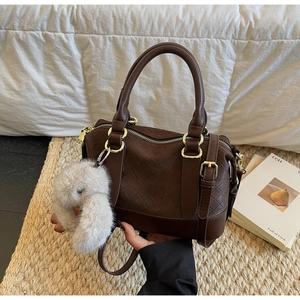Close-up of a dark brown woven tote bag featuring a plush bunny charm and gold hardware