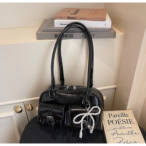 Detail of glossy black shoulder bag featuring dual front pockets and pearl bow charm