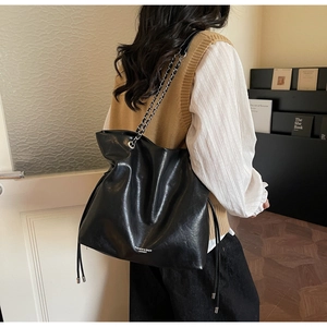 Detail view of large black leather tote bag with chain strap and drawstring design