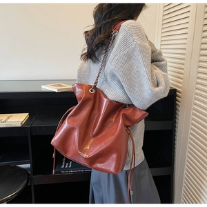 Side view of reddish-brown drawstring bucket bag with silver chain and pleated texture
