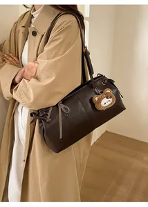 Detail of coffee brown leather tote bag featuring a cute plush bear charm and bow detail