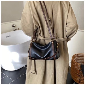 Detail of minimalist retro crossbody bag with black leather and brown strap on a beige coat