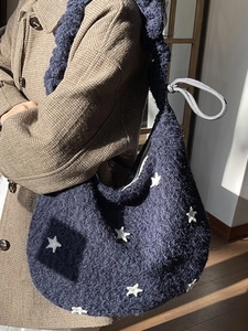 Blue knit shoulder bag with white star patterns and wide strap in casual indoor setting