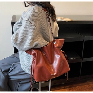 Detail view of large brown leather tote bag with silver chain strap and drawstring design