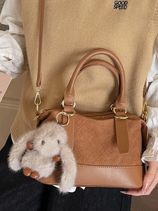 Brown woven Boston bag with rabbit charm, worn over shoulder with a long strap