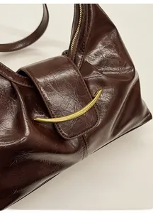 Gros plan du sac baguette en cuir ciré marron foncé avec boucle dorée incurvée