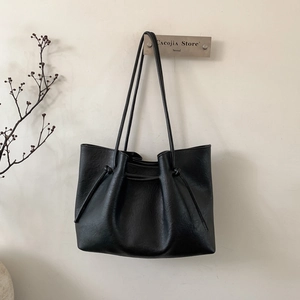 Detail of minimalist black leather tote bag with drawstring knots and slender shoulder strap