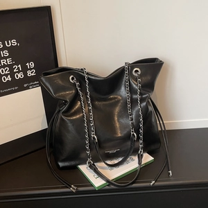 Close-up of black leather tote bag featuring silver chain straps and side drawstring details