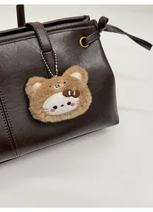 Detail of cute brown plush bear charm with embroidered cat face on leather tote bag