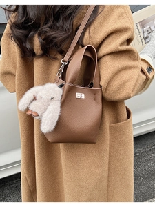 Detail of dark brown leather bucket bag with metal lock and plush rabbit charm