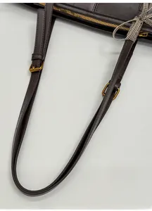Detail of dark brown bag with adjustable leather straps, gold buckles and ribbon