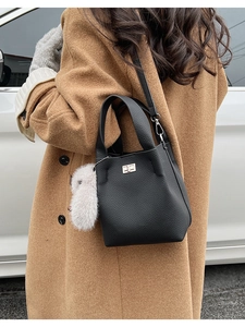 Detail of black lychee grain leather bucket bag with silver buckle and white fur pompom charm