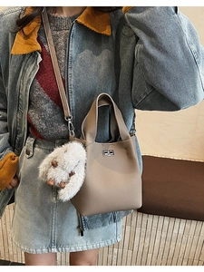 Detailed close-up of lychee grain leather bucket bag with silver lock and plush charm