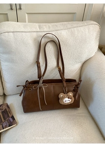 Detail view of retro brown leather bag with a cute bear pendant and plaid bow on sofa