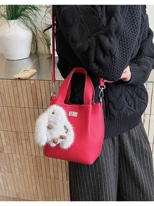 Close-up of red lychee textured bucket bag with silver lock and plush bunny charm