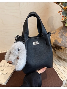 Detail of black pebbled leather bucket bag featuring silver twist lock and plush rabbit charm