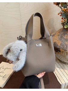 Close-up of litchi texture leather bucket bag with silver twist lock and plush charm