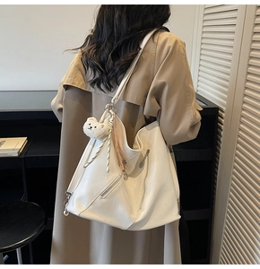 Détail d'un grand sac cabas blanc crème avec un ours en peluche sur l'épaule d'un mannequin