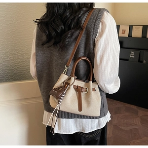 Detail of a beige canvas bucket bag with brown leather trim worn by a model in casual style