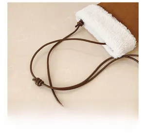 Detail of plush faux fur trim on a brown suede crossbody bag with adjustable rope strap