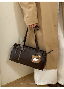 Detail of dark brown leather crossbody bag with a cute bear charm and gold hardware