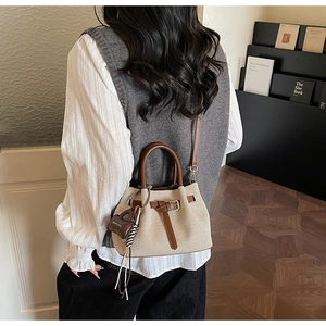 Detail view of canvas bucket bag with brown leather trim and chic mini charm