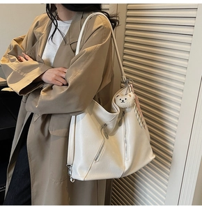 Détail d'un cabas en cuir blanc avec fermeture éclair argentée et pendentif ours en peluche