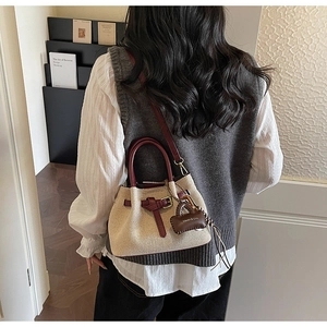 Detailed close-up of woven bucket bag featuring burgundy leather strap and brand charm