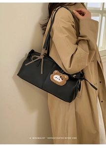 Close-up of black leather rectangular shoulder bag with plush bear charm and bow detail