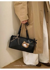 Detail view of retro black leather tote bag with elegant bow and plush bear charm