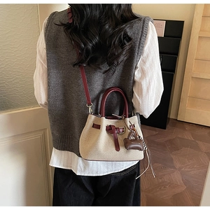 Detail of beige woven bucket bag with burgundy leather straps and a mini charm