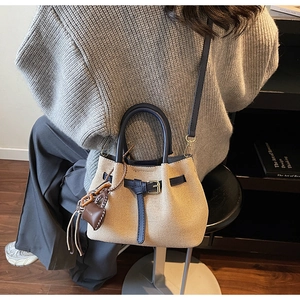 Detail showing woven texture and navy leather straps of a beige bucket handbag