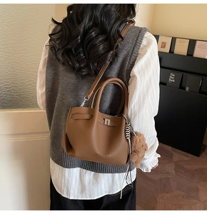 Détail d'un sac seau en cuir marron avec motif litchi et pendentif ours en peluche