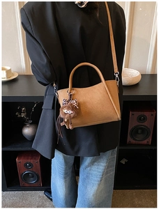 Detail of light brown PU leather bucket bag with cute plush monster charm on a model