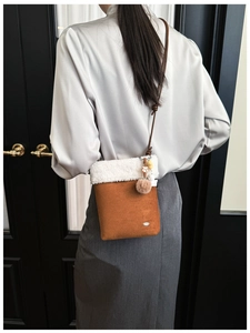 Detail of caramel suede crossbody bag with white faux shearling trim and pompom pendant