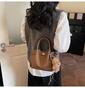 Sac seau en cuir grainé marron porté par un mannequin avec un charm d'ours
