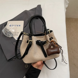 Detail of canvas and leather bucket bag with brand charm and premium metal hardware accents