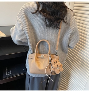 Détail d'un sac seau beige avec boucle métallique et pendentif ours en peluche