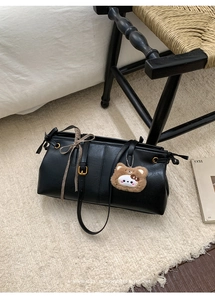 Detail of black PU leather shoulder bag featuring a cute bear pendant and ribbon strap