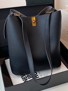 Minimalist black pebbled leather bucket bag with gold clasp shown in a luxury gift box