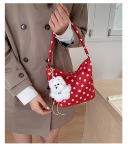 Detail view of red polka dot hobo bag with a plush puppy charm on a khaki coat