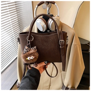 Detail of dark brown leather tote bag with plush charm and shoulder strap hardware