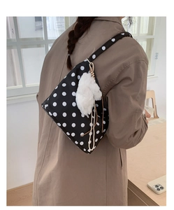 Detail of black canvas shoulder bag with white polka dots and a fluffy white pompom charm