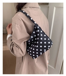 Polka dot shoulder bag shown on shoulder of model wearing a stylish tan trench coat