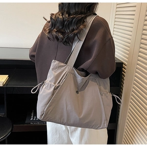 Detail of a large capacity nylon tote bag with side drawstring pockets on a model